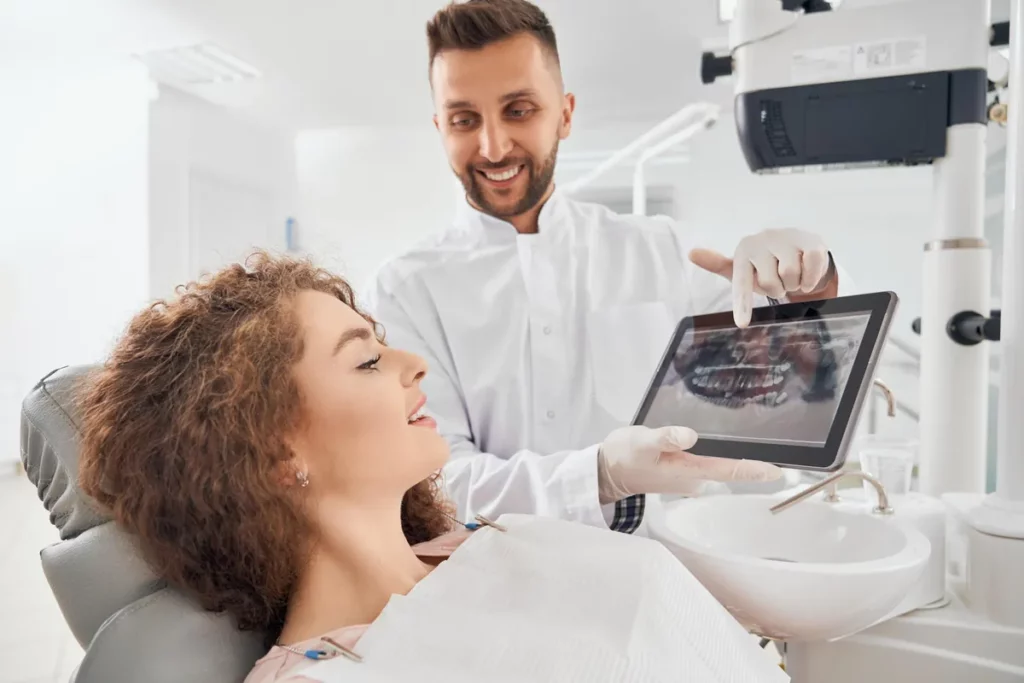 Dentiste souriant montrant une radio panoramique sur tablette à une patiente installée au fauteuil