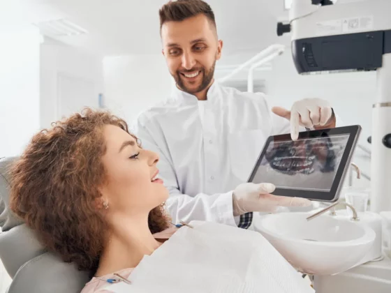 Dentiste souriant montrant une radio panoramique sur tablette à une patiente installée au fauteuil