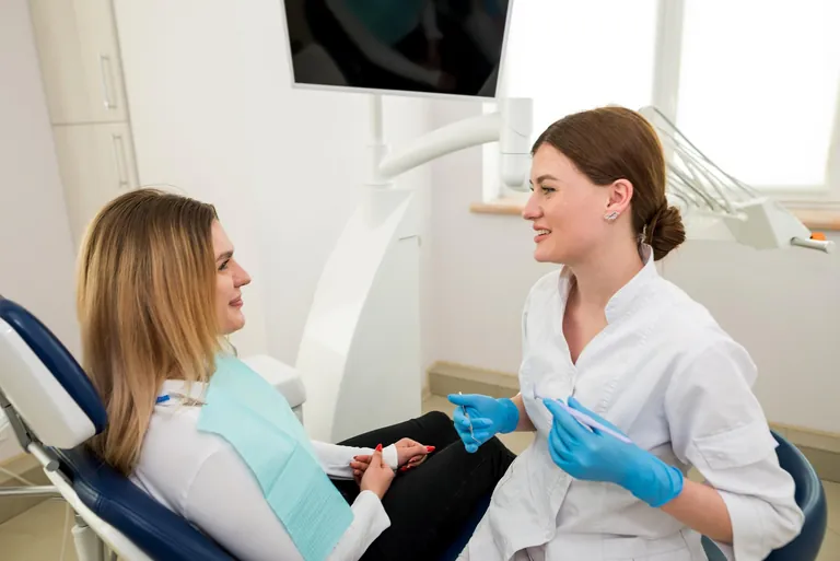 Chirurgienne-dentiste en blouse blanche échangeant avec une patiente assise au fauteuil dentaire