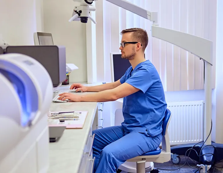 Chirurgien-dentiste en tenue bleue travaillant sur un ordinateur dans son cabinet dentaire