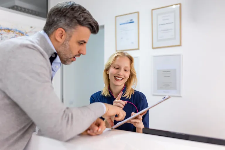 Patient remplissant un formulaire avec l’assistante à l’accueil d’un cabinet